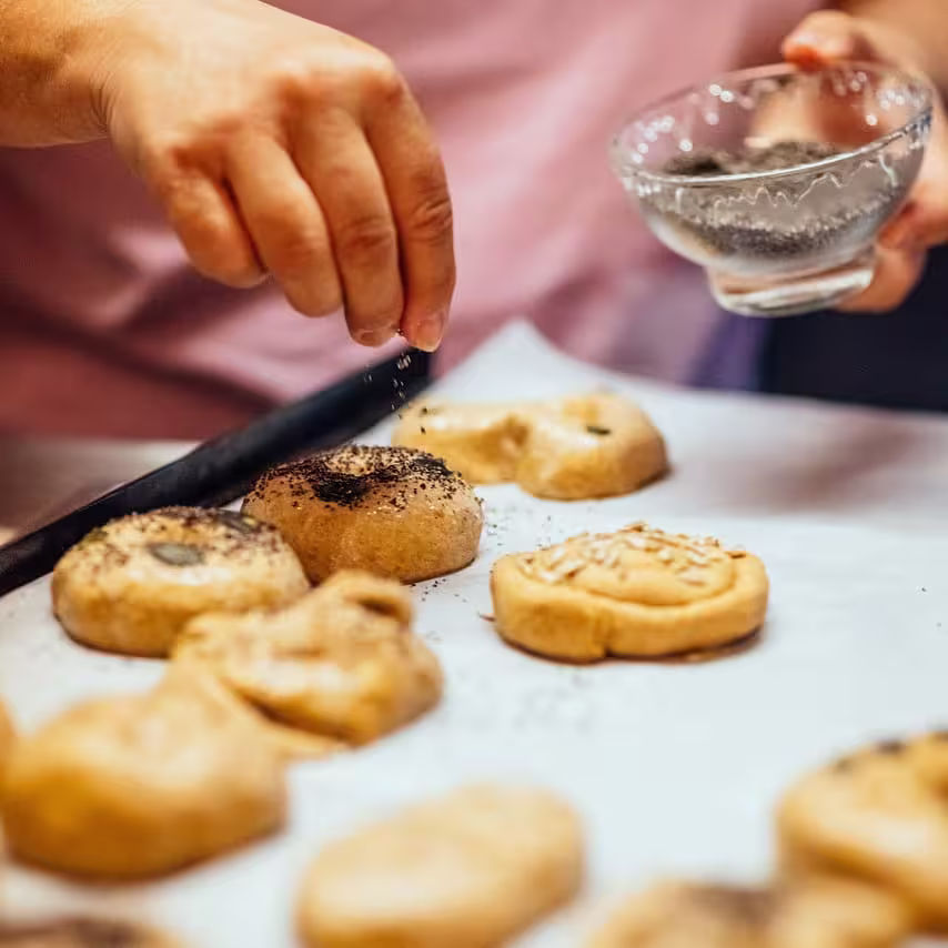 Baker sprinkling poppy seeds and ground Grains of Paradise mix on top of freshly baked pastries